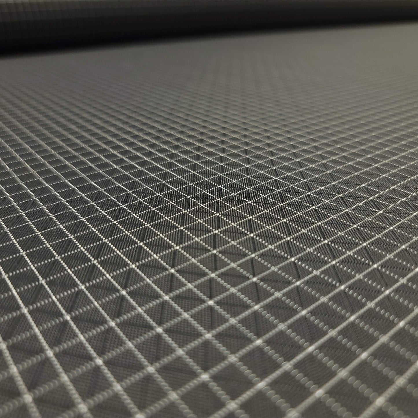 High-quality image showcasing my Charcoal Grey 210D UHMWPE Gridstop Nylon fabric, emphasizing its lightweight, durable woven texture and unique waterproof properties. The image highlights the fabric's intricate UHMWPE fiber grid, its robust 210D denier thickness, and the dual protective coating – 1000mm PU on the back and DWR on the front. Ideal for visualizing the fabric's application in making resilient, weather-resistant outdoor gear like backpacks, fanny packs, and reinforcement areas.